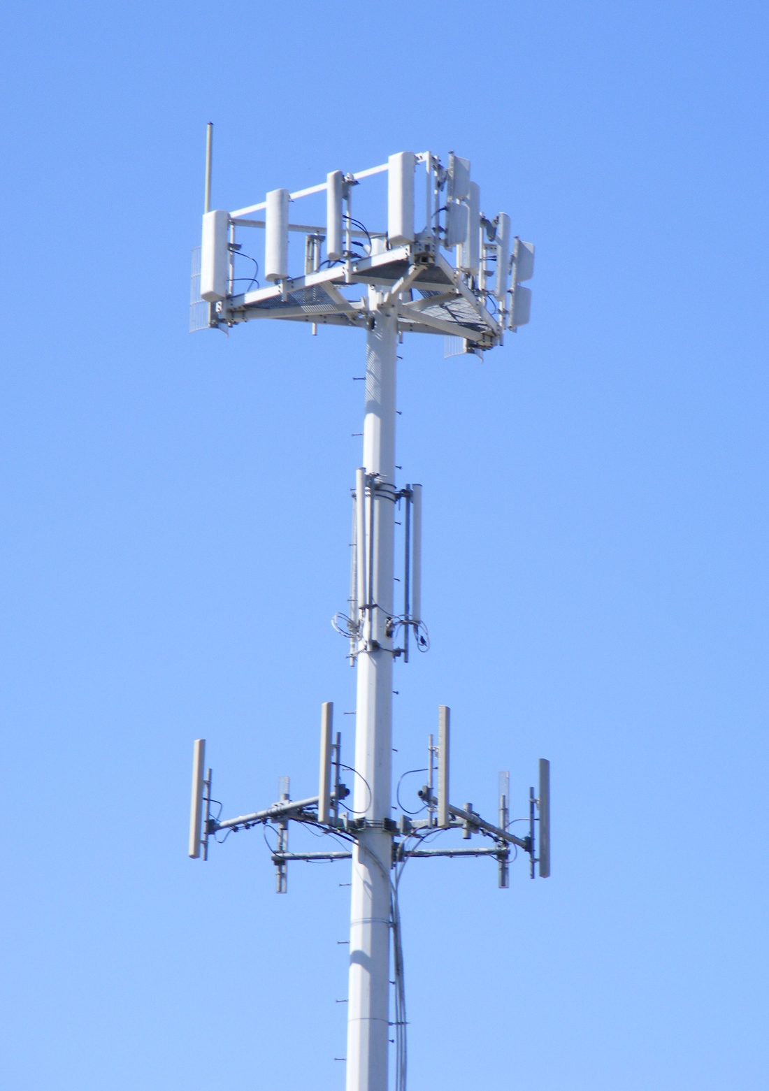 Bir hücresel baz istasyonu kulesinin tepesi: dikdörtgen panel antenler farklı yönlere bakacak biçimde direğe dizilmiş. Her panelin baktığı yön ayrı bir hücre demek, ve yürürken bağlantın bu panellerden biriyle diğeri arasında devrediliyor.