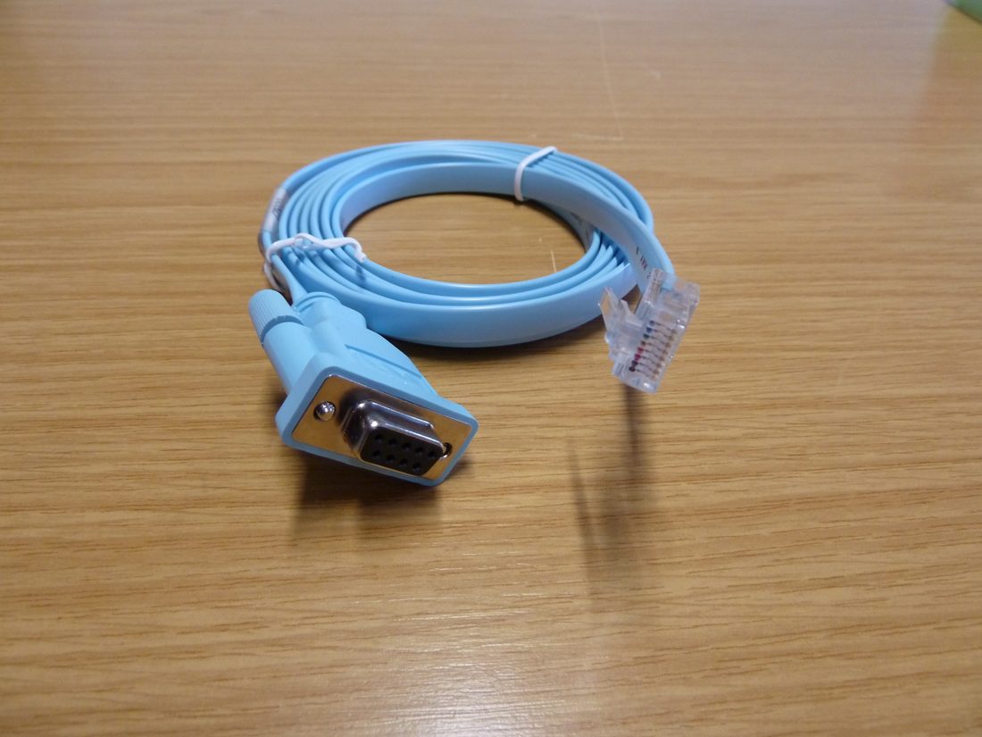 Bir ucunda RJ-45 fişi, öbür ucunda seri konnektör bulunan açık mavi Cisco konsol kablosu. Ağ portuna değil cihazın yönetim yuvasına takılan, ağ tümüyle çöktüğünde ayakta kalan tek fiziksel yol.